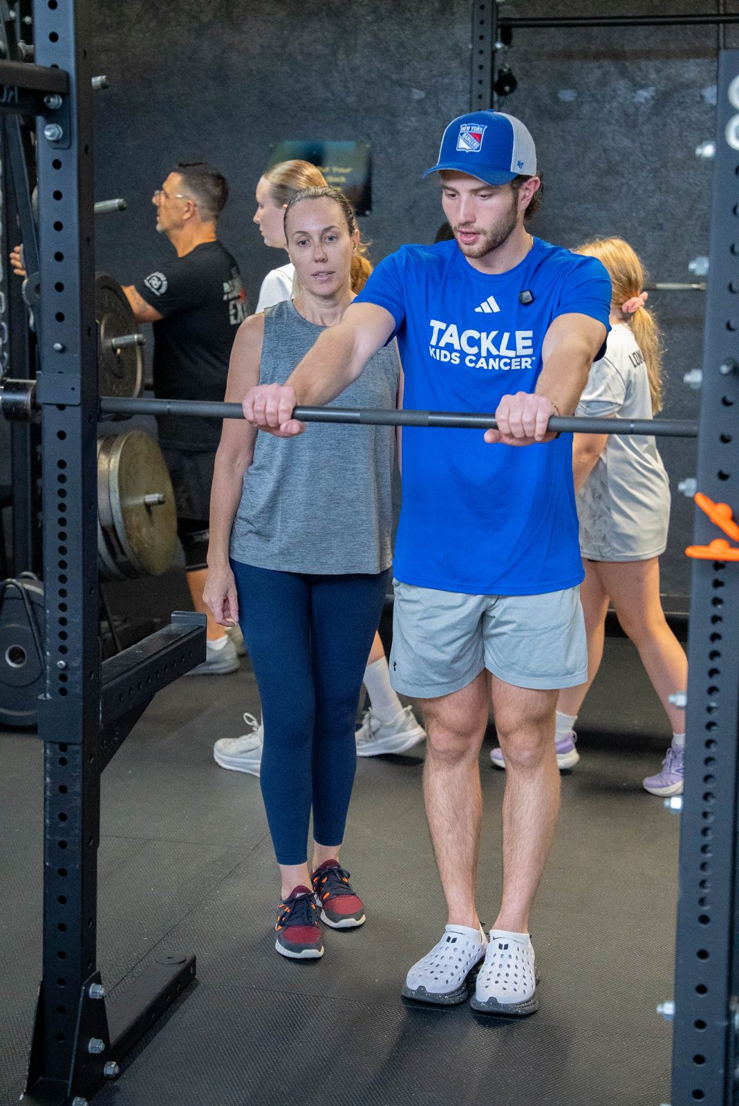 Coach demonstrating barbell position to an adult member during small-group strength training at RAF