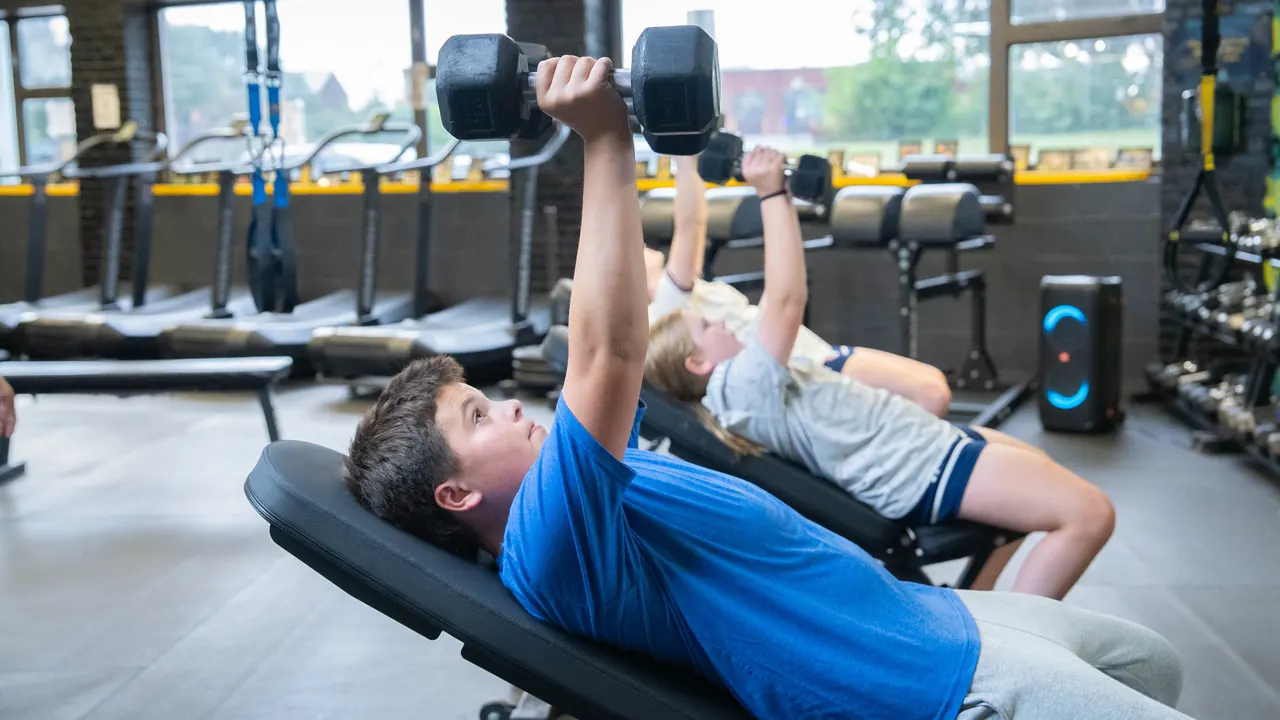Teen athlete pressing dumbbells during RAF youth strength training